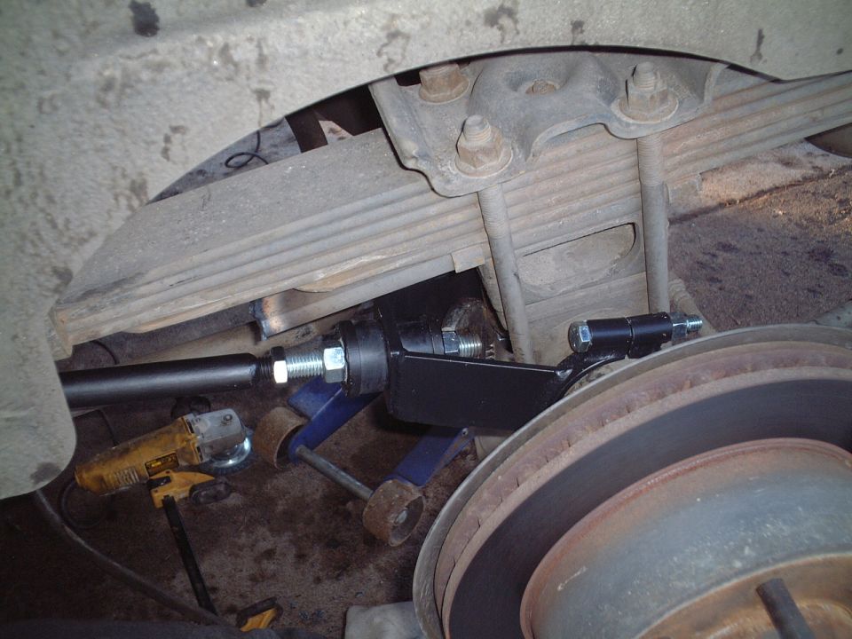 Leaf spring suspension underside with U-bolts, rotor, and DeWalt grinder during install