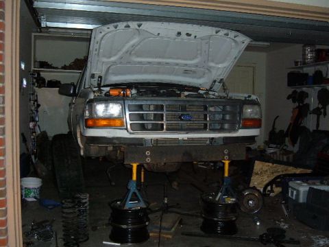 1993 Ford Bronco - Front view of a white Ford Bronco being worked on in a garage, with its hood up and front end elevated.