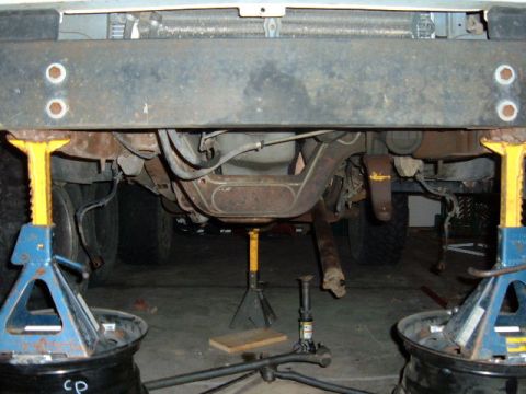 1993 Ford Bronco - The front suspension and exhaust system of a 1993 Ford Bronco are visible while it is elevated on jack stands.