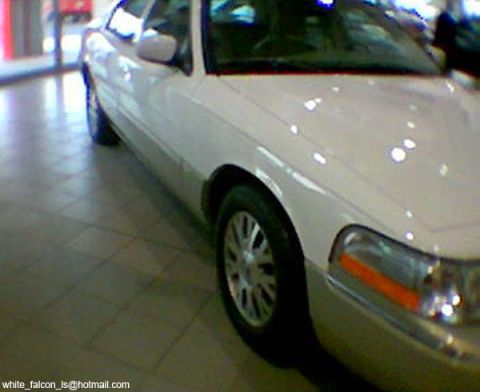 1999 Mercury Grand Marquis - This white sedan is parked indoors on a tiled floor, showing its front corner and wheel.