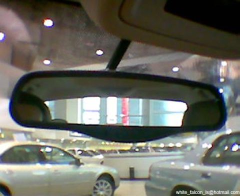 1999 Mercury Grand Marquis - Reflection in the rearview mirror shows multiple vehicles in a showroom setting.