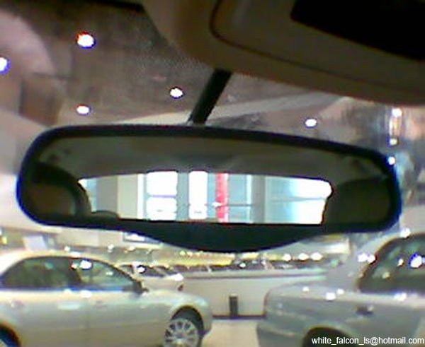 Interior rearview mirror reflecting a showroom with cars and lights