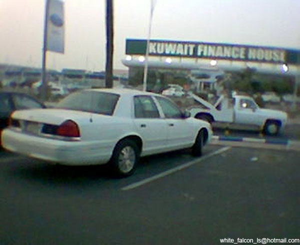 White sedan parked next to a white tow truck. Kuwait Finance House sign in background