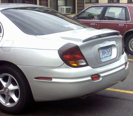 2002 Oldsmobile Aurora - Rear view of a silver sedan with a spoiler, parked in a lot next to another vehicle.