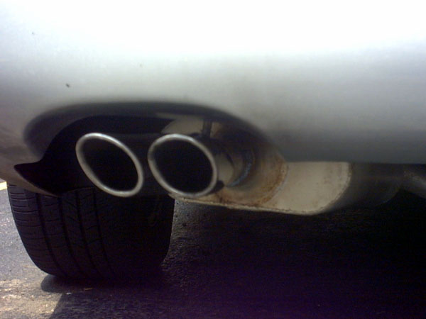 Close-up of dual chrome exhaust tips under a silver car's rear bumper beside the tire