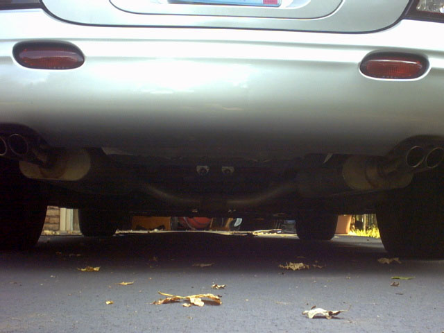 Underbody rear view of a silver sedan showing dual exhaust routing and rear bumper from below
