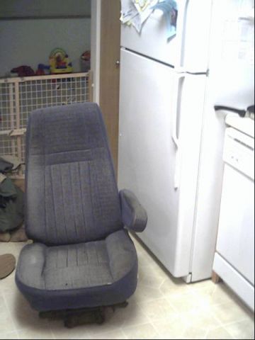 1987 Ford Bronco - A single car seat is positioned in a room with a refrigerator and a baby gate in the background.
