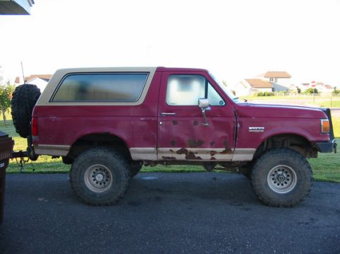 1989 Ford Bronco - This is a side view of a red Ford Bronco with a tan removable hardtop and a spare tire mounted on the rear.