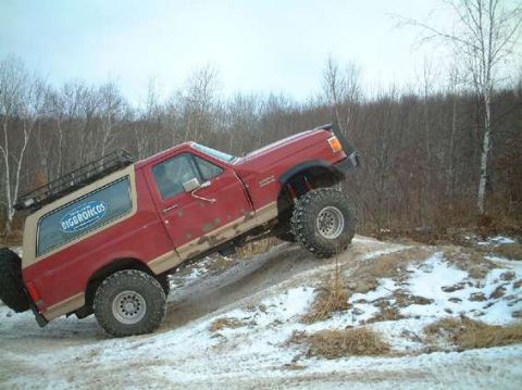 1989 Ford Bronco - This red Ford Bronco is shown off-roading in a snowy environment.