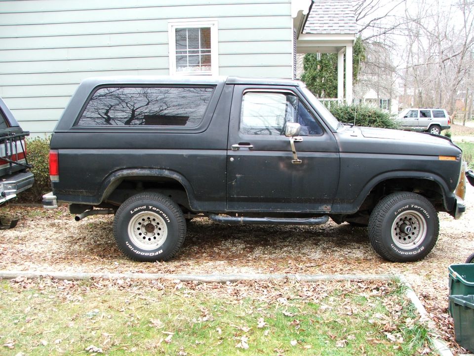 Black two-door Ford Bronco SUV in side view parked on leafy lawn by a house