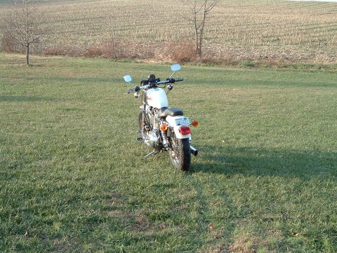 1995 Mercury Grand Marquis - A white motorcycle is parked in a grassy field with a dry cornfield in the background.
