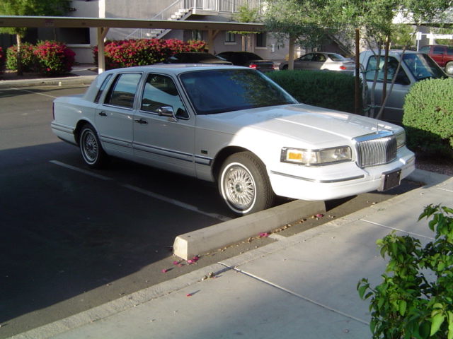 White Lincoln Town Car sedan parked in apartment lot, front three-quarter passenger view