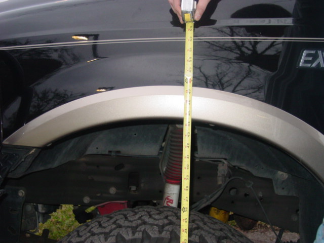 Tape measure gauging wheel well height on black SUV with gold fender flare