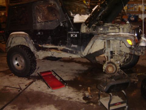 1992 Ford Bronco - A Jeep Wrangler is undergoing maintenance in a garage, with the hood open and a wheel removed.