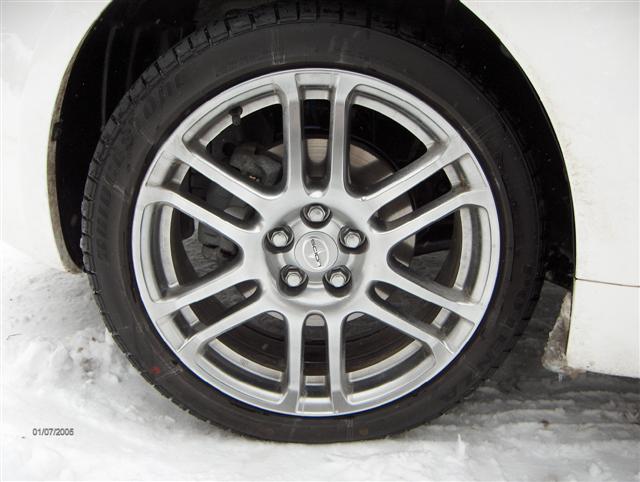 Close-up of silver alloy wheel with Bridgestone tire on white Scion, parked in snow