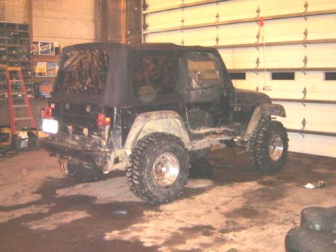 1992 Ford Bronco - A black Jeep Wrangler with a soft top and off-road tires is parked inside a garage.