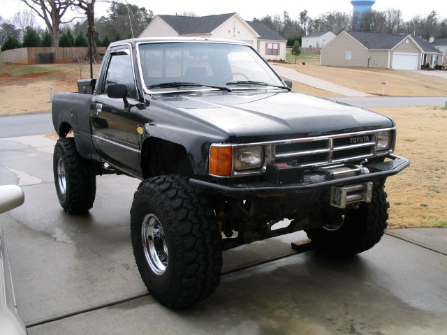 Black Toyota pickup truck with lifted suspension and large tires. Has a winch on the front bumper