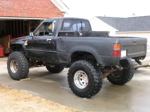 1986 Ford F-150 - This lifted Toyota pickup truck has large off-road tires and a toolbox mounted in the bed.