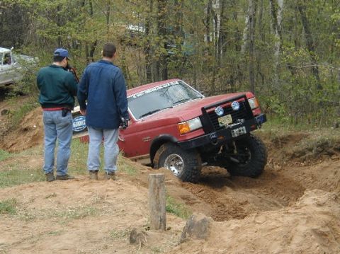 1989 Ford Bronco - Two men observe a red off-road vehicle navigating a challenging dirt terrain.