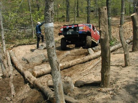 1989 Ford Bronco - A red off-road vehicle is shown traversing a challenging course with logs and rocks.