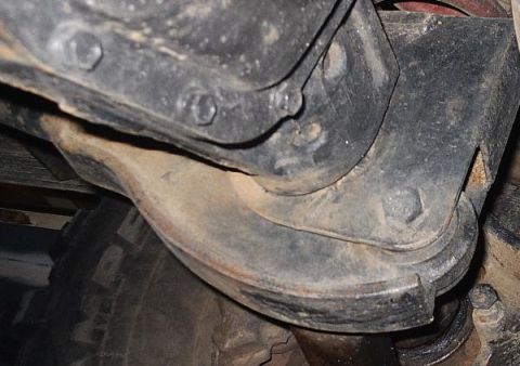 1996 Ford Bronco - Underside view of vehicle suspension parts, including brackets and bolts, with a tire visible.