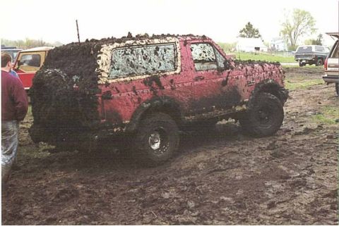 1989 Ford Bronco - A red SUV is heavily covered in mud, suggesting it has been off-roading.