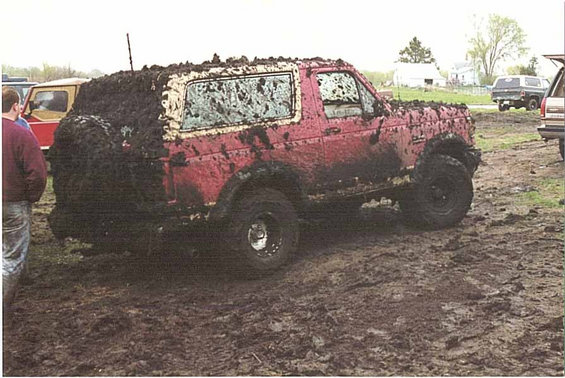 Red SUV covered in mud, seen from the rear quarter angle, with a spare tire on the back