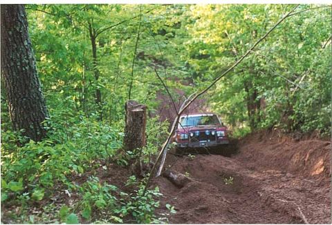 1989 Ford Bronco - Jeep Cherokee XJ navigates a challenging dirt path through a wooded area.