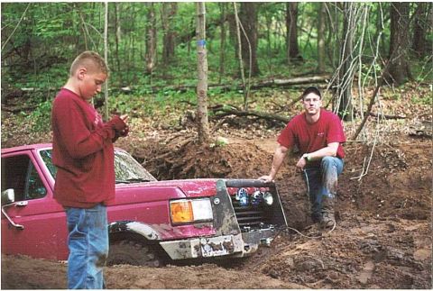 1989 Ford Bronco - A red Ford truck is stuck in the mud with two people standing around it.