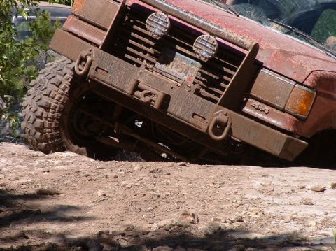 1989 Ford Bronco - This heavily muddied off-road vehicle navigates a rough terrain, its front end angled upwards.
