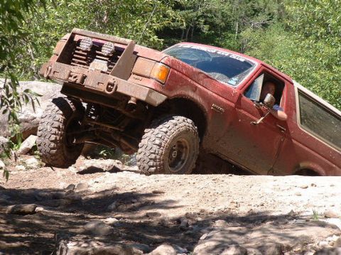 1989 Ford Bronco - This red 1989 Ford Bronco is navigating a difficult off-road course with large rocks and dirt.
