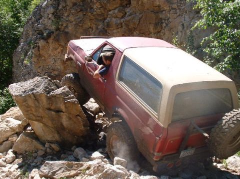 1989 Ford Bronco - This vehicle is attempting to climb over large rocks on a trail, showing its off-road capabilities.