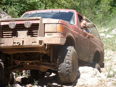 1989 Ford Bronco - A red Ford Bronco navigates a challenging rocky terrain with a driver visible inside.