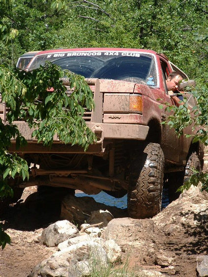 1989 Ford Bronco - A red 1987 Ford Bronco tackles a challenging off-road course, its tires gripping rocks and mud.