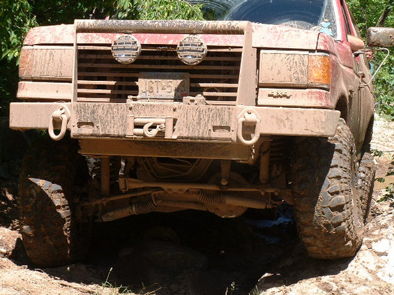 1989 Ford Bronco front grille and bumper covered in mud, with winch and auxiliary lights