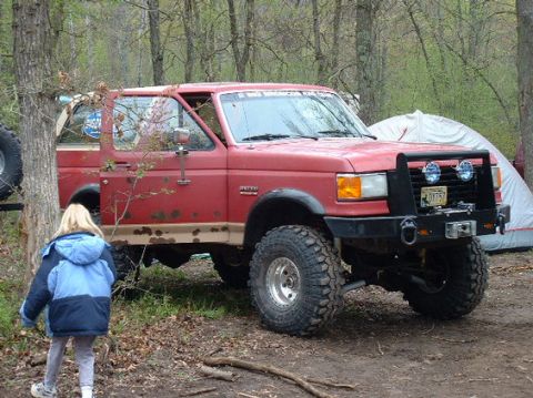 1989 Ford Bronco - This red SUV, possibly a Ford Bronco, is equipped for off-road adventures and is parked at a campsite.