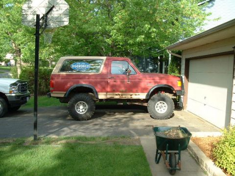 1989 Ford Bronco - This red 1989 Ford Bronco features a tan top, off-road tires, and a "BIGBRONCOS" decal on the rear window.