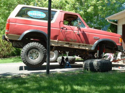 1989 Ford Bronco - Red 1989 Ford Bronco is lifted on jack stands for repairs, showing its suspension and lifted stance.