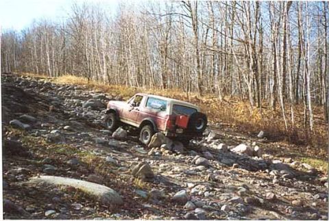 1989 Ford Bronco - Ford Bronco navigating a challenging rocky trail in a wooded area.