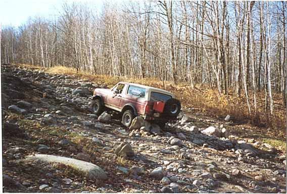 Red Ford Bronco climbing a rocky hill with bare trees in the background