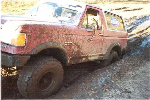 1989 Ford Bronco - This red Ford Bronco is deeply embedded in thick mud, with its tires struggling for traction.