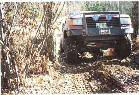 1989 Ford Bronco - This 1989 Ford Bronco is captured from the rear, navigating a challenging off-road trail with a winch and custom bumper visible.
