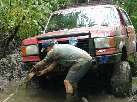 1989 Ford Bronco - A person attempts to free a red 1987 Ford Bronco from deep mud.