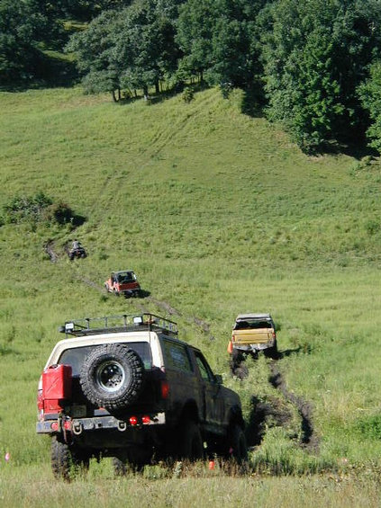 1989 Ford Bronco - Multiple off-road vehicles navigate a challenging, muddy incline on a sunny day.