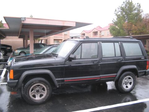1991 Ford Bronco - A black Jeep Cherokee is parked on a wet surface next to other vehicles.