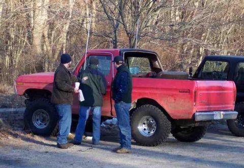 1978 Ford Bronco - Three men stand around a red pickup truck parked outdoors near trees.