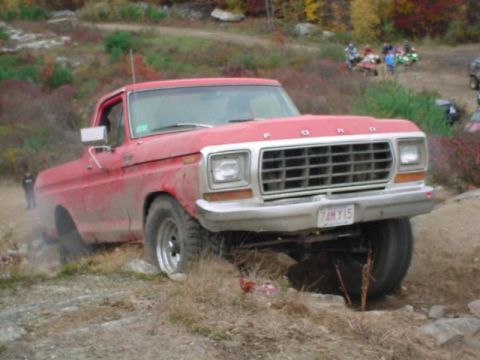 1978 Ford Bronco - A red Ford pickup truck navigates a rocky off-road trail with other vehicles visible in the background.