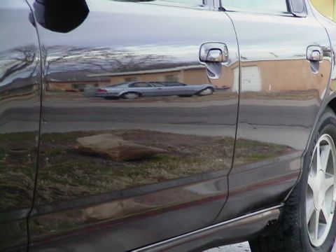 1995 Ford Contour - Reflection of a silver sedan, possibly from the 1990s, is visible on the dark-colored car's door.