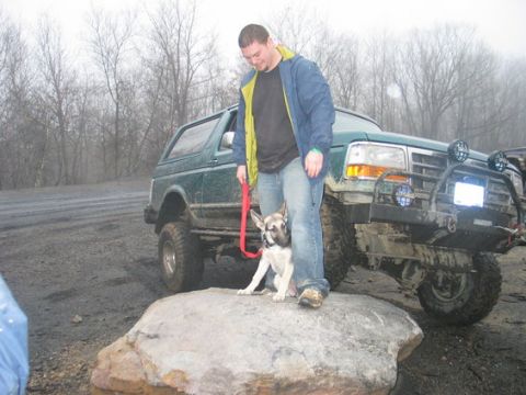 1990 Ford Bronco - Man and dog pose with a lifted green Ford Bronco on a rocky, off-road terrain.