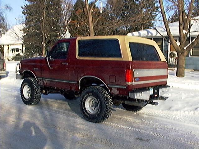 Red and tan lifted Ford Bronco SUV, rear quarter view, parked on snowy street